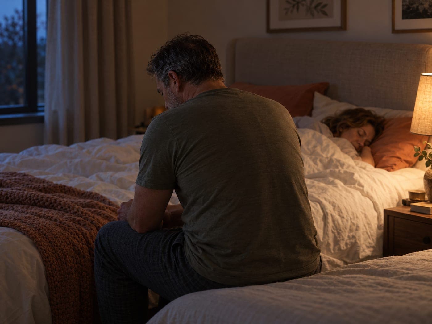 A man sitting on the edge of a bed at night